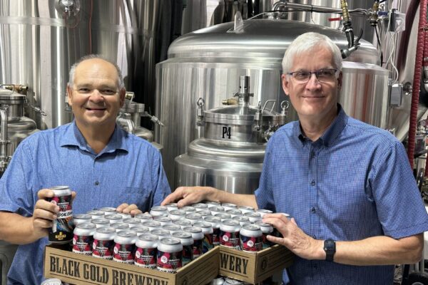 Executive Director, Dave Brown, and board member, Alan Blahey pose in front of several cases of United Way branded beer at Black Gold Brewery