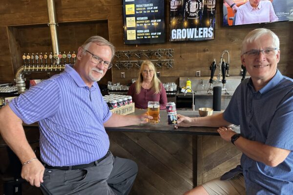 Former United Way board member, Al McChesney, poses in front of a case and glass of United Way branded beer with current board member, Alan Blahey