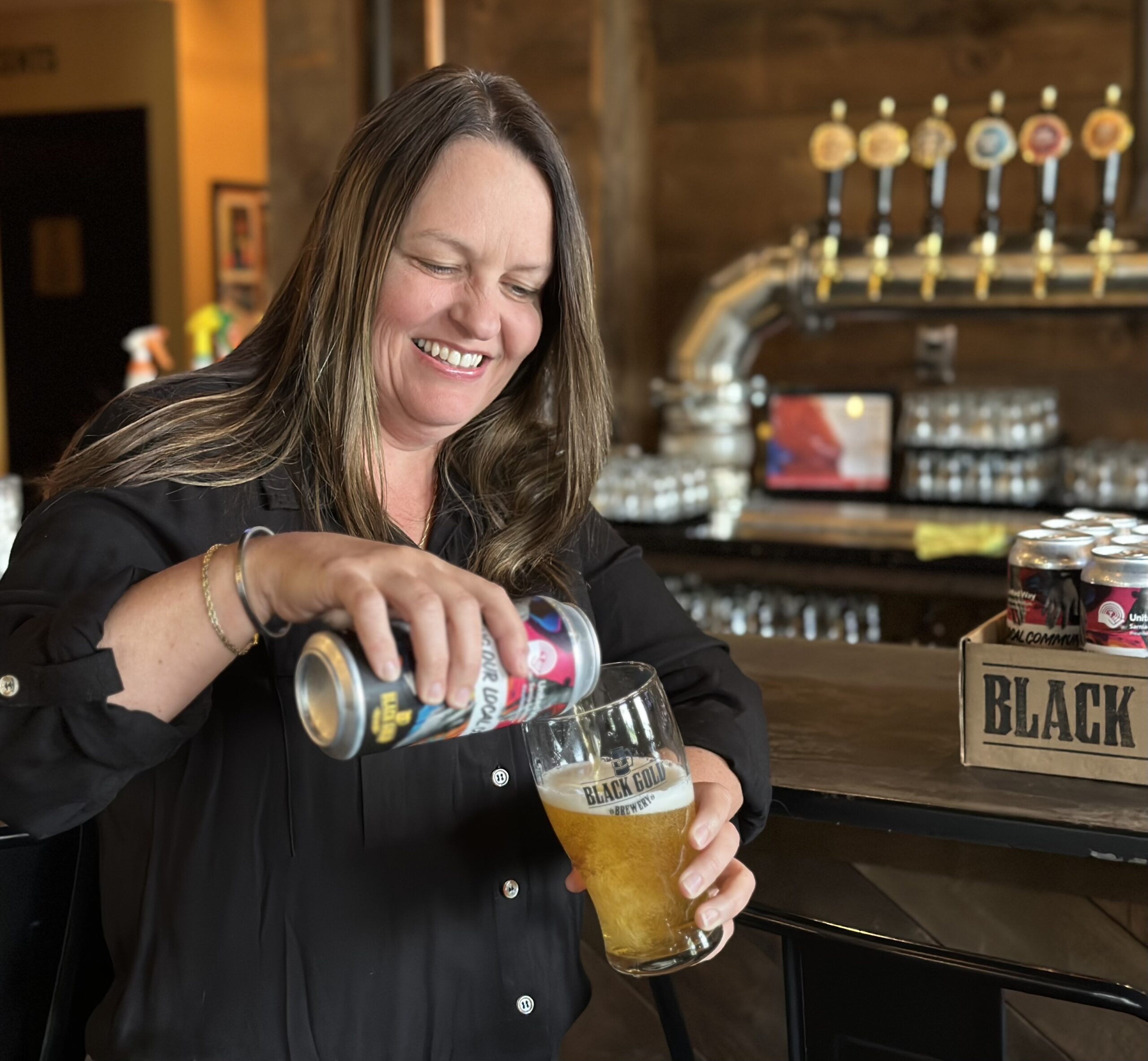 Board member Krista pours a glass of United Way branded beer at Black Gold brewery
